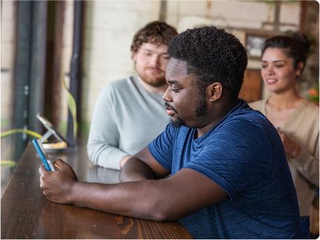 A man on his phone sits at a dark wood table