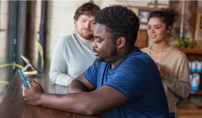 A man on his phone sits at a dark wood table