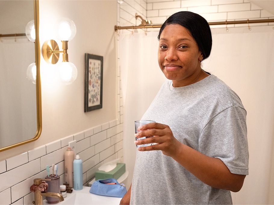 A smiling woman stands in a white bathroom next to a sink