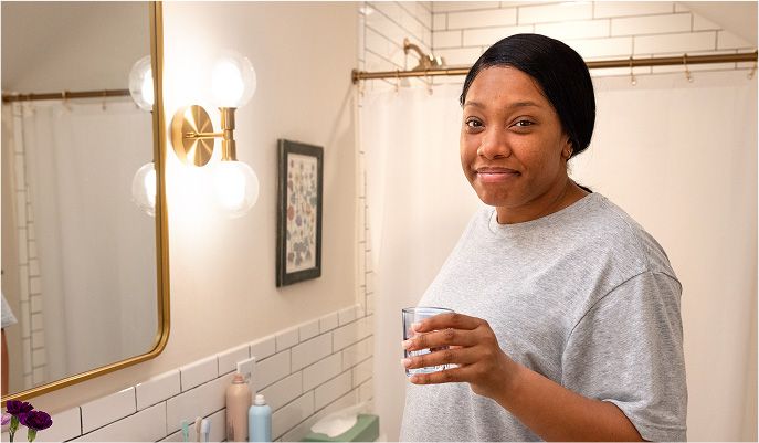 A smiling woman stands in a white bathroom next to a sink
