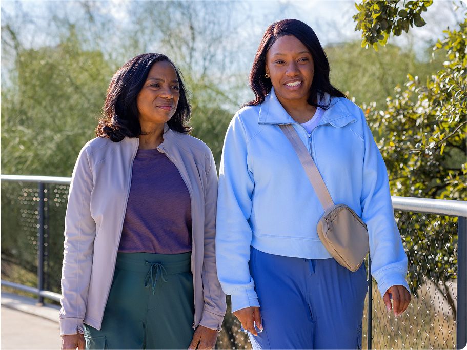 Two women walk side by side on a road outside while talking