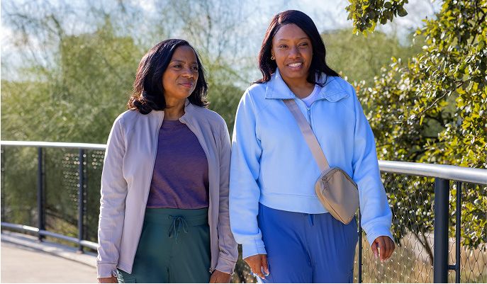 Two women walk side by side on a road outside while talking