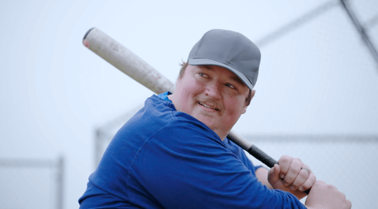 Avary, an actual COBENFY (xanomeline and trospium chloride) patient, getting ready to swing a baseball bat