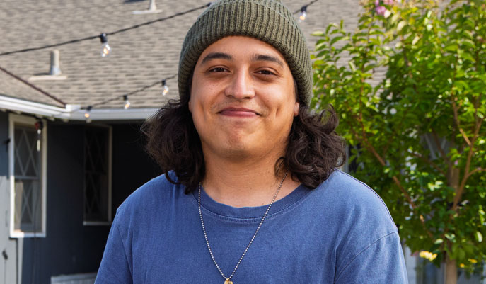 Portrait of Bryan, an actual COBENFY (xanomeline and trospium chloride) patient, wearing an olive green beanie and blue t-shirt
