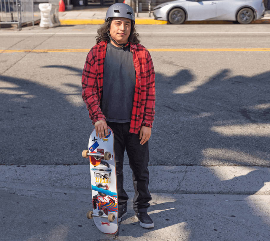 Bryan, an actual COBENFY (xanomeline and trospium chloride) patient, stands in front of a street with a skateboard