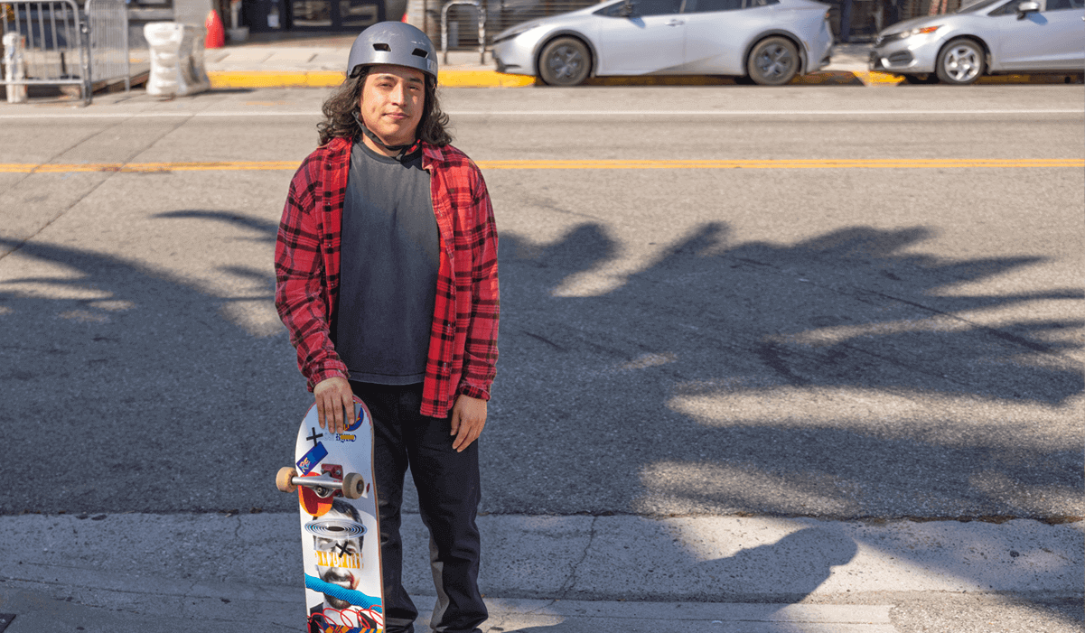 Bryan, an actual COBENFY (xanomeline and trospium chloride) patient, stands in front of a street with a skateboard